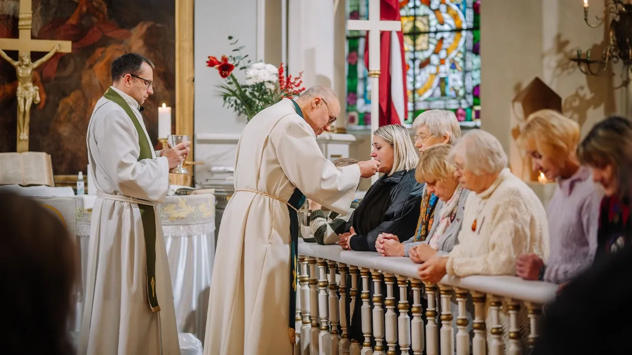 Priest distributing communion wafer to a woman kneeling at the altar rail during a church service.