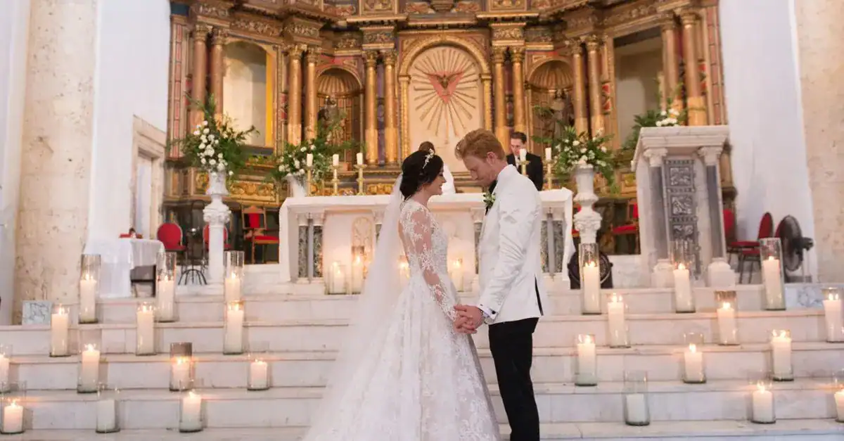 Bride and groom holding hands at the altar of a decorated Catholic church during their wedding ceremony.